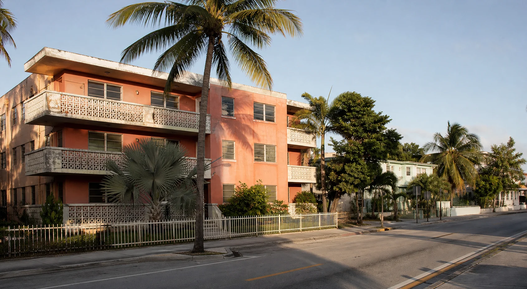 A coral mid-century apartment building on a palm-lined Miami street